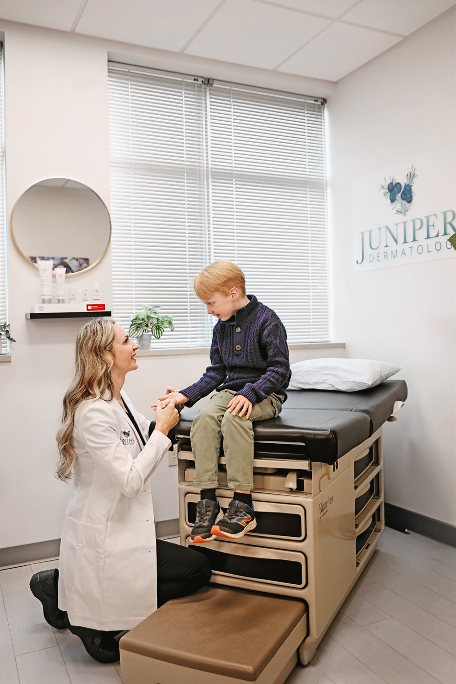 A Juniper Dermatology dermatologist kneeling to meet a young boy at his level during a friendly skin visit in Bend, Oregon
