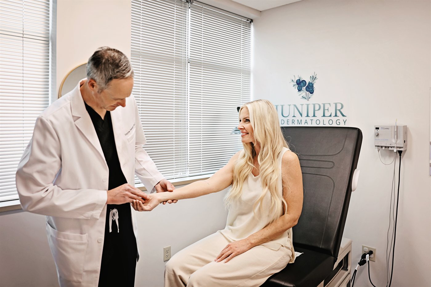 A Juniper Dermatology clinician examining a smiling patient's arm during a skin cancer screening in Bend, Oregon