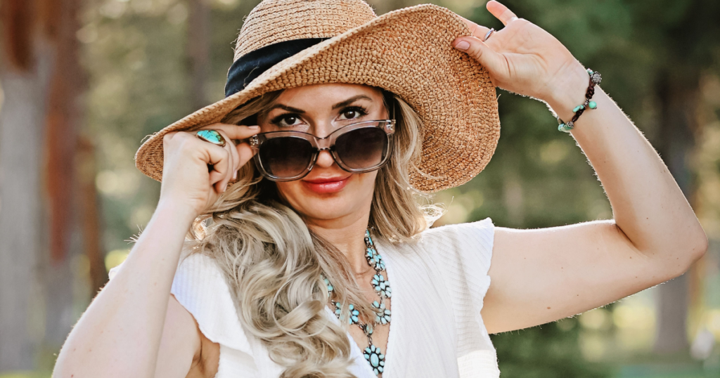 Woman peeking over sunglasses and wearing a sun hat.