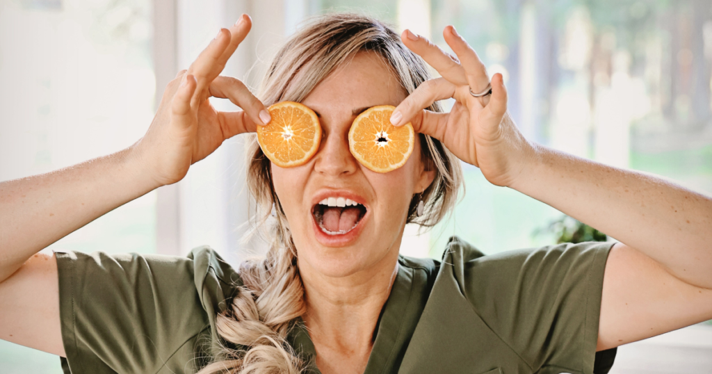 Woman holding orange slices over her eyes.